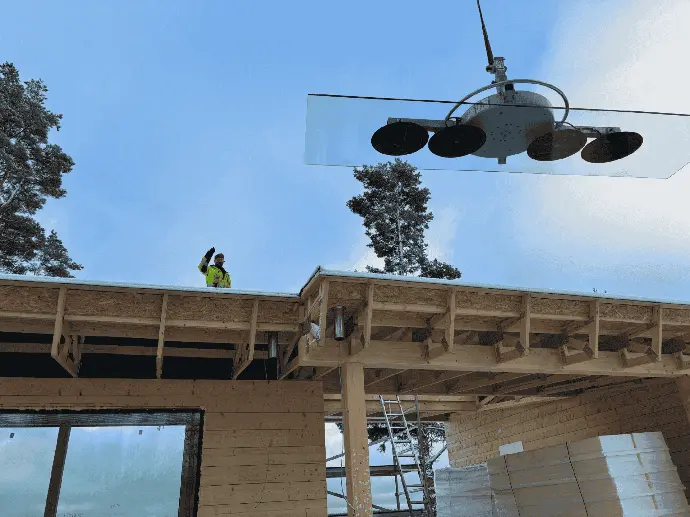 Rakennustyömaa, jossa suuri lasielementti nostetaan katolle.